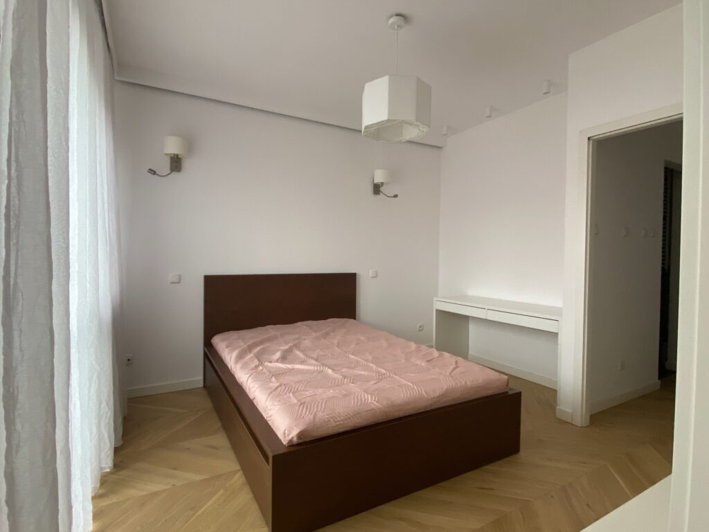 Minimalistyczna sypialnia z białymi ścianami i drewnianym łóżkiem