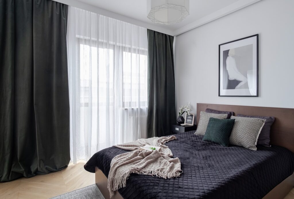 Elegancka sypialnia z ciemnymi zasłonami i czarną narzutą po home stagingu.