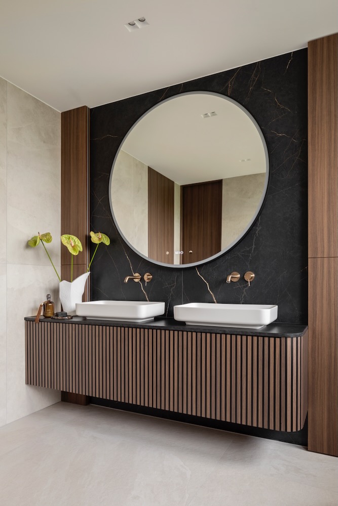 Łazienka z dwoma umywalkami, okrągłym lustrem i czarno-drewnianą zabudową
