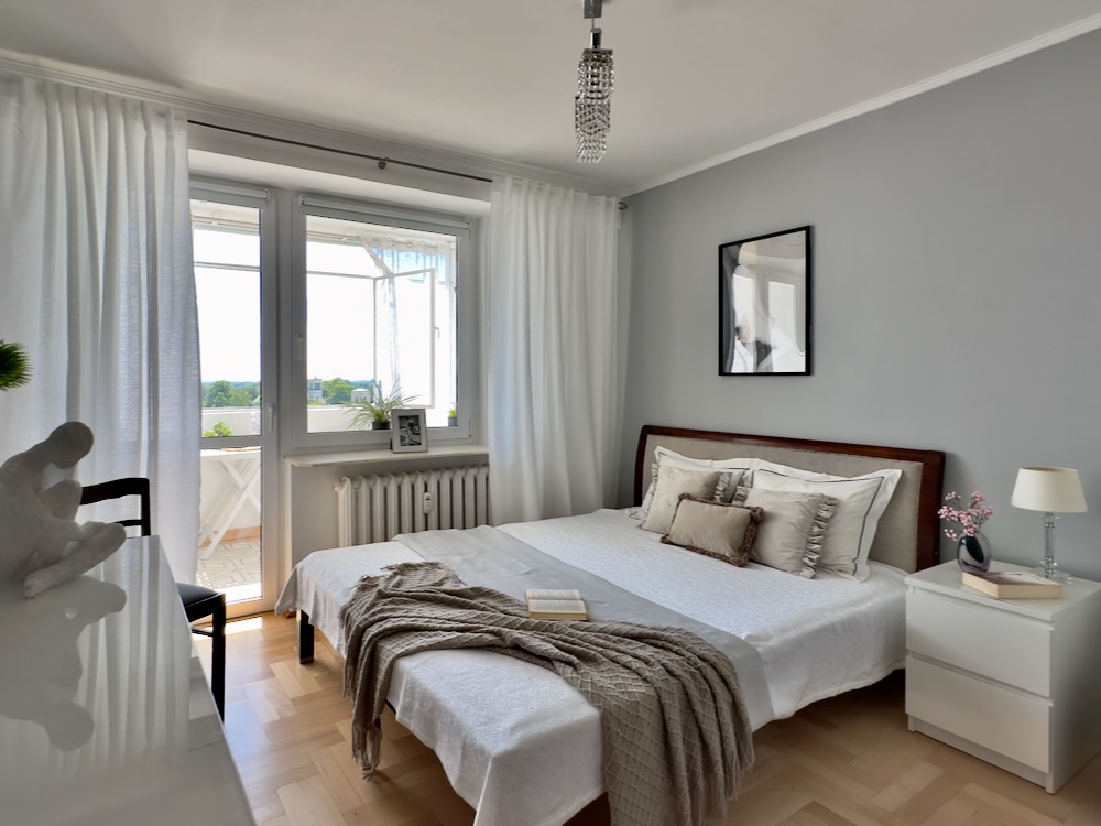 Sypialnia z białymi zasłonami i wyjściem na balkon