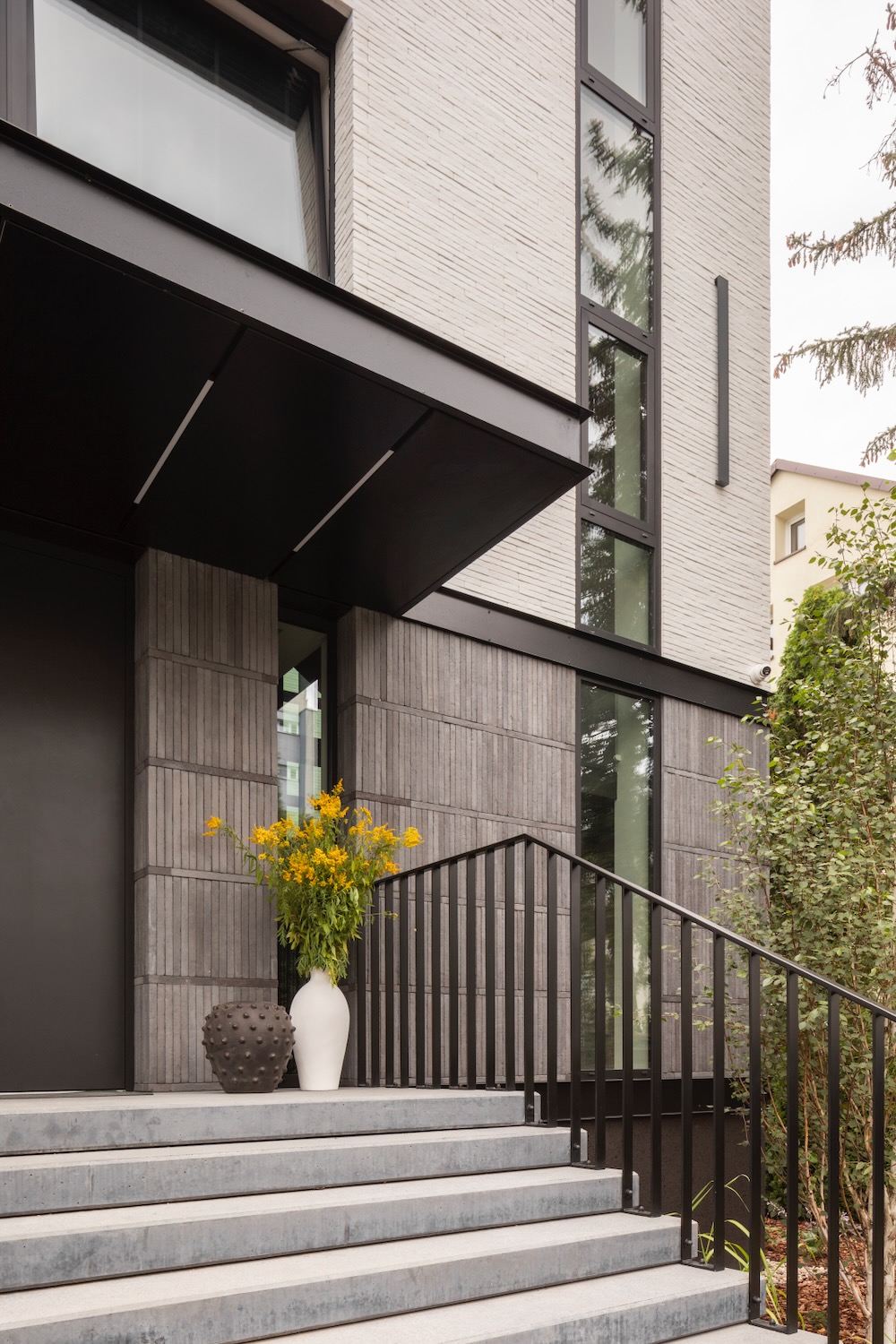 Nowoczesne wejście do domu z czarną elewacją i kwiatami w białych wazonach