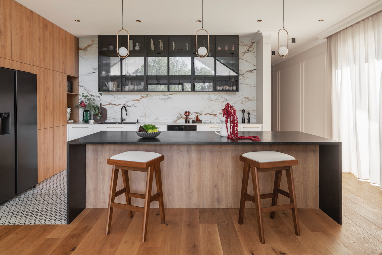 Nowoczesna kuchnia z wyspą po homestagingu: drewniane fronty, marmurowy backsplash i designerskie hokery w apartamencie w Warszawie